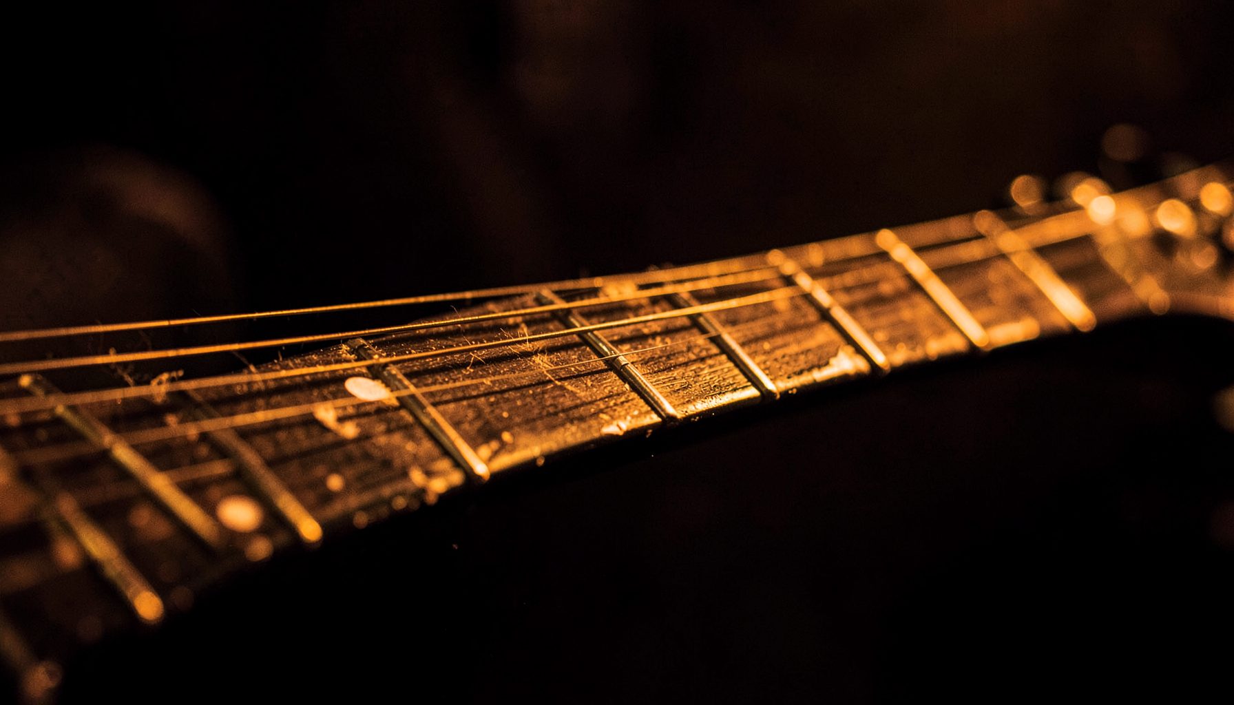 Close-up of a worn electric guitar neck and strings under warm amber stage light, moody and intimate