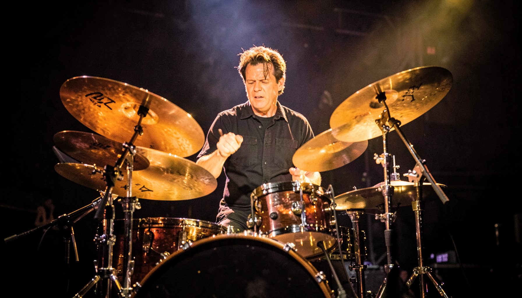 Drummer behind a kit, cymbals catching warm stage light, energetic rock-show atmosphere
