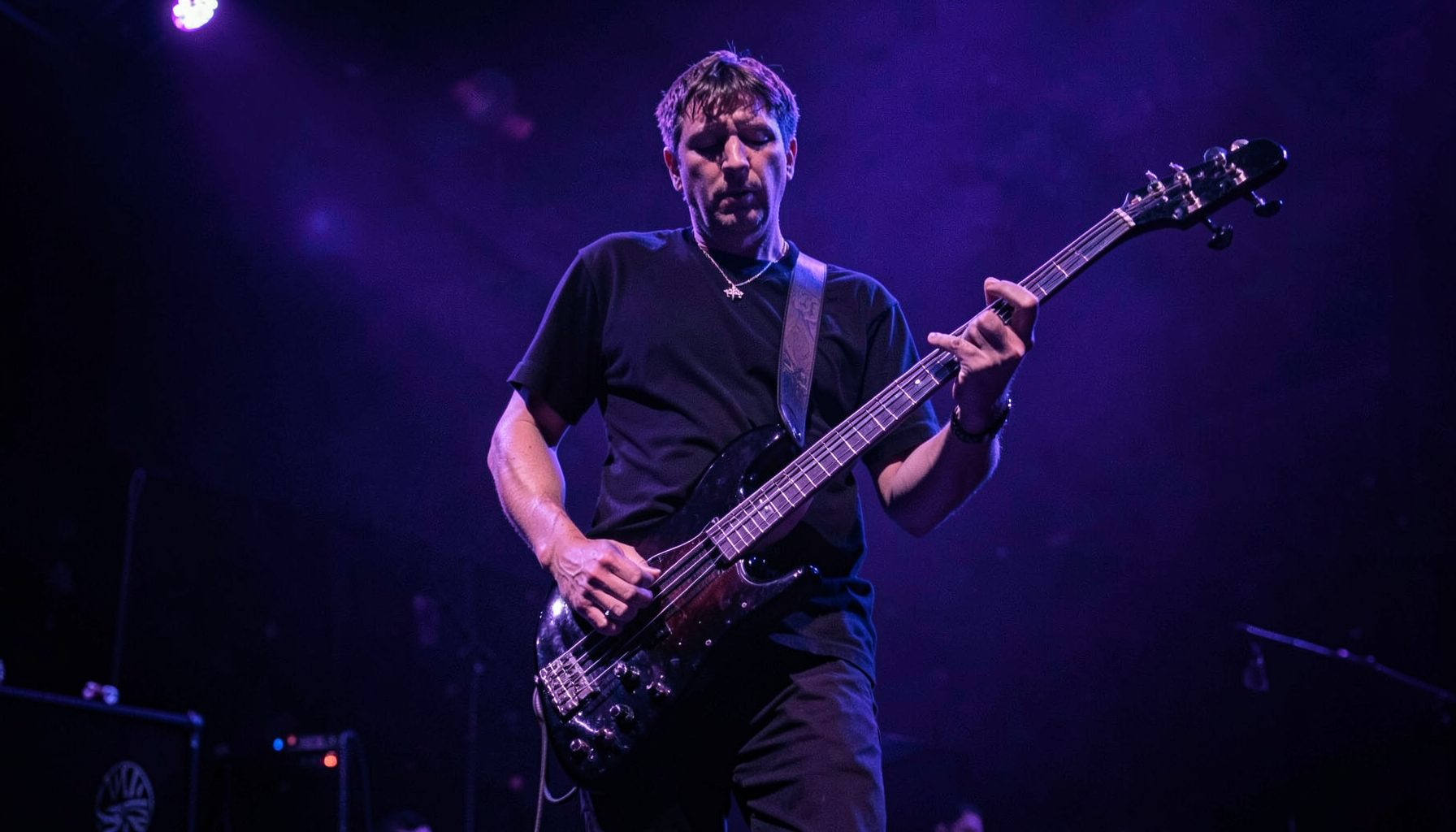 Bass player on stage with deep purple and cool blue lighting, low-slung bass guitar