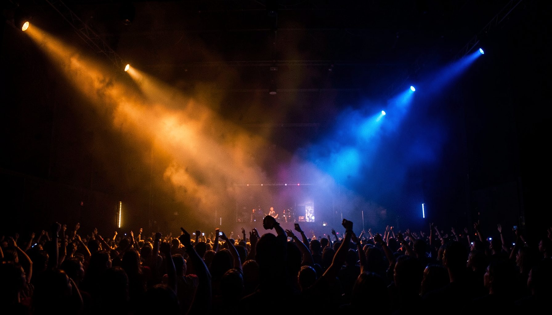 Dark stage with amber and blue spotlights cutting through haze, a rock-concert atmosphere