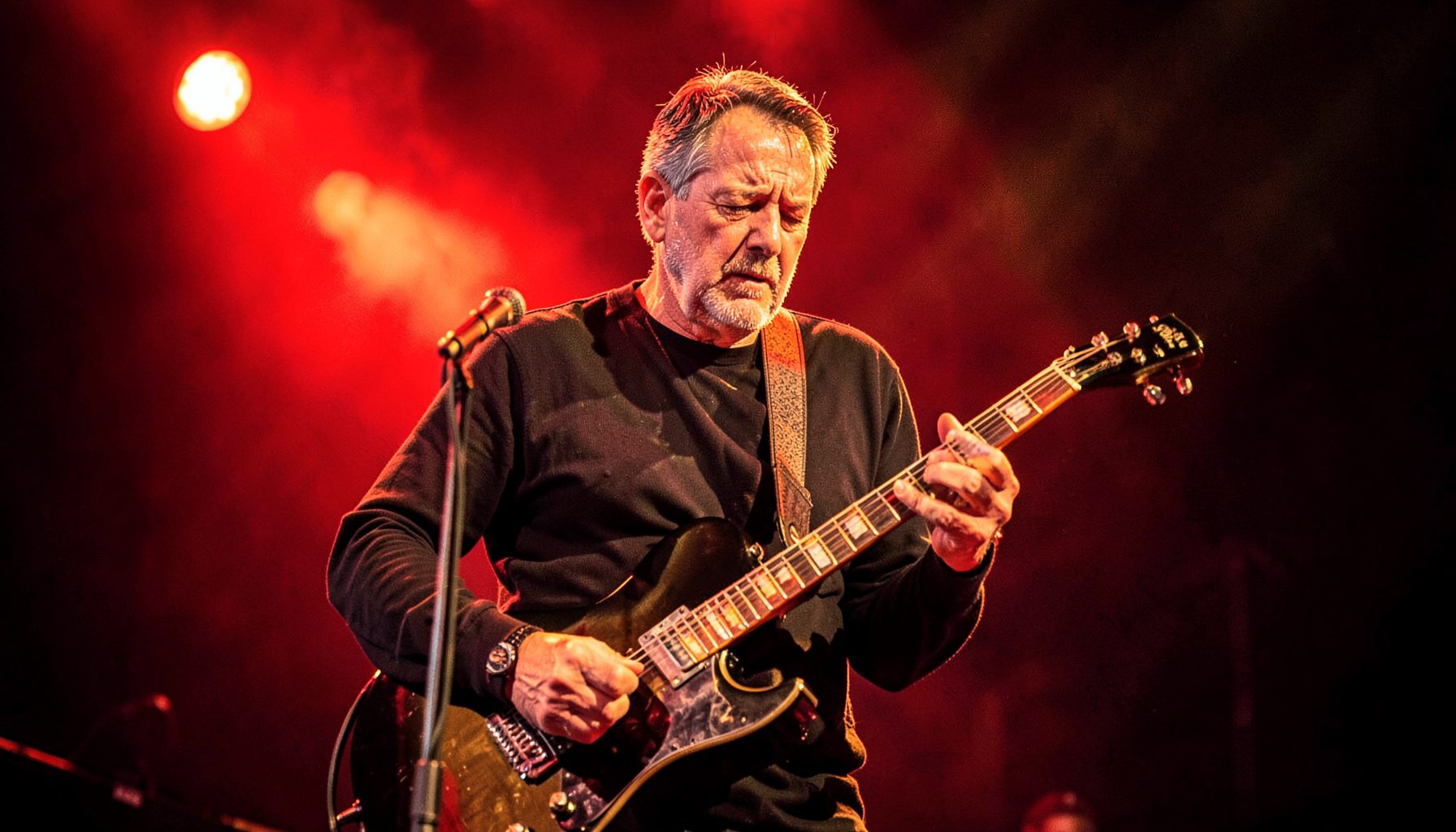 Rhythm guitarist performing under stage lights, rich red and gold hues, focused expression