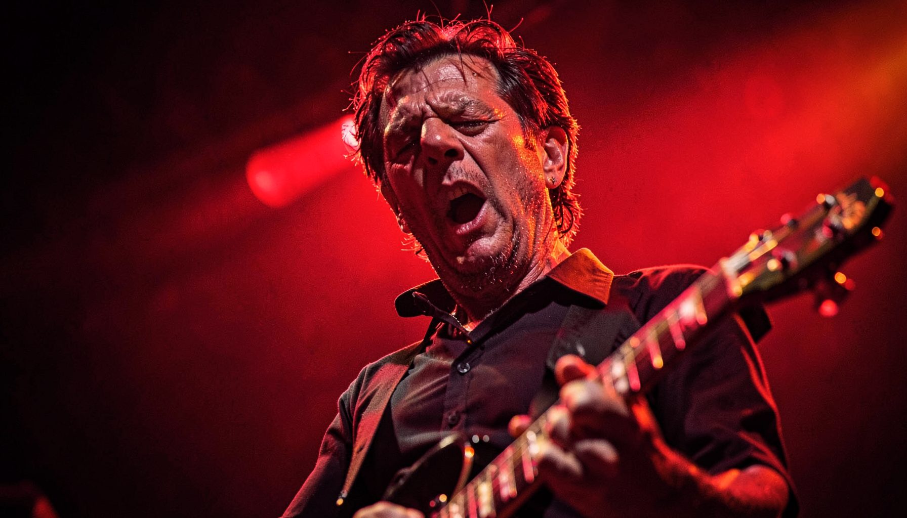 Close-up of a guitarist on stage under red and amber lights, intense expression, low-angle perspective